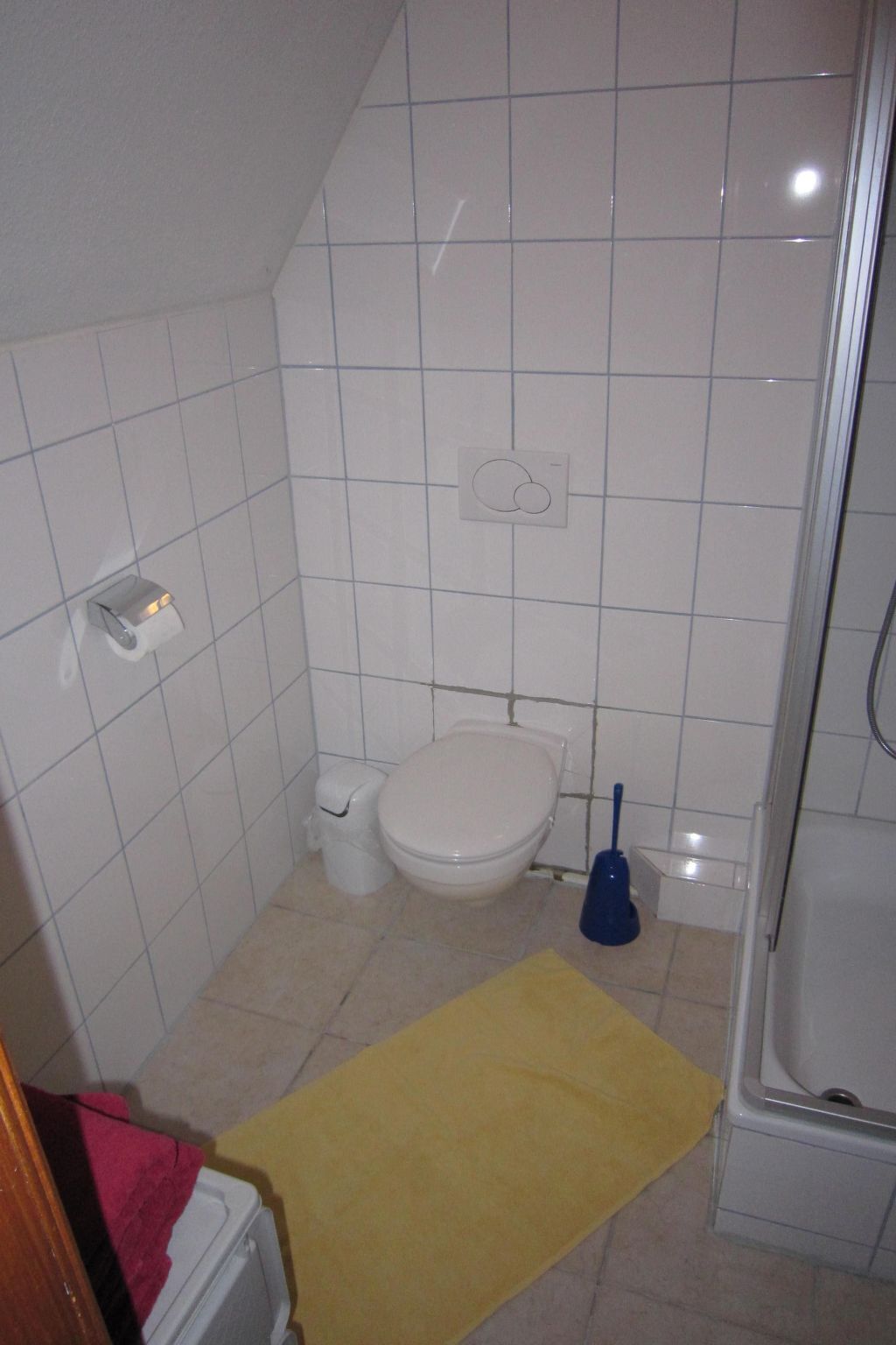 Pieni, siisti kylpyhuone, jossa on valkoiset laatat, wc, bidee ja suihkutila.