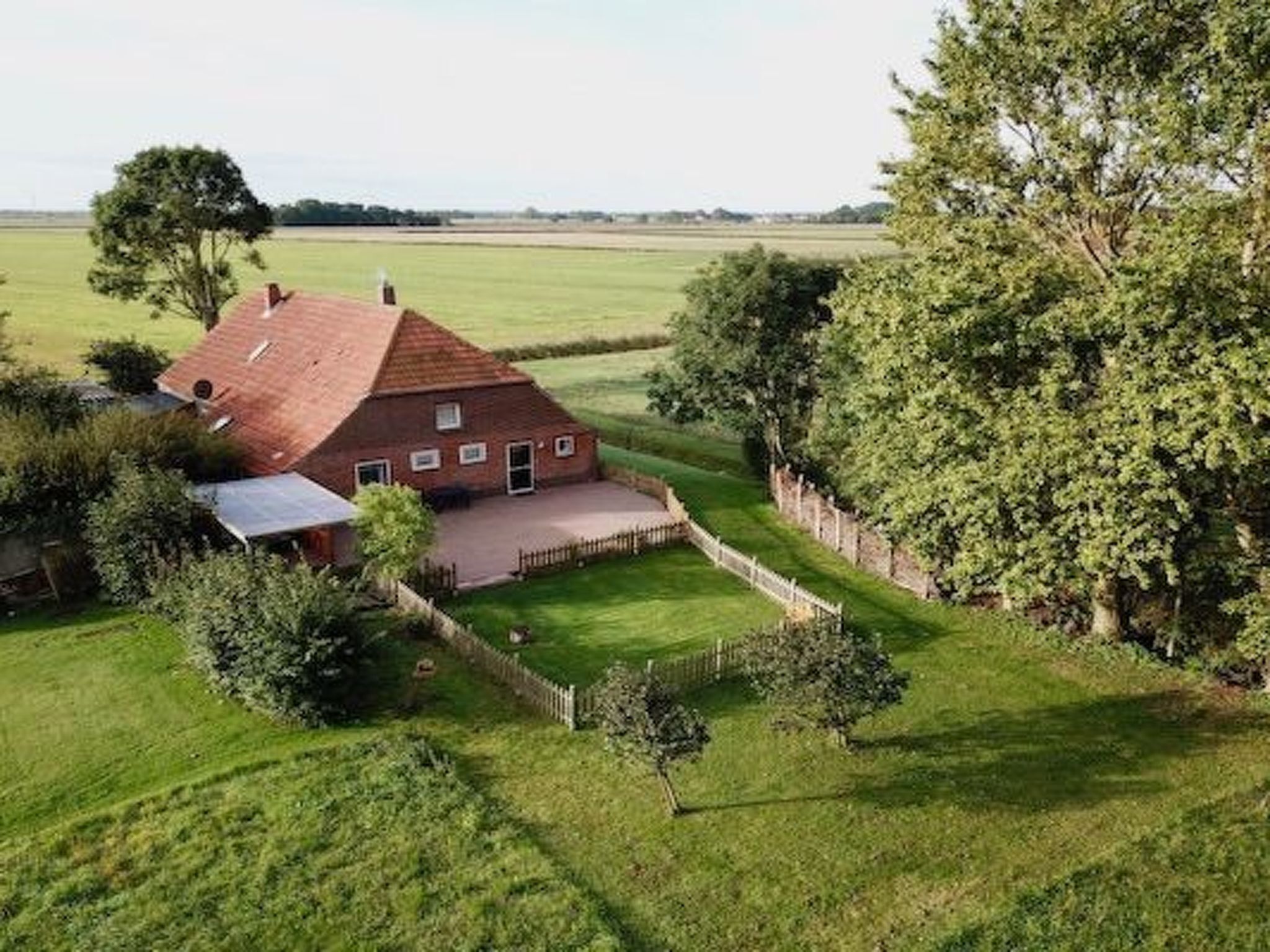 Een groot huis met een schuin dak, omgeven door een verzorgd gazon en een houten hek.