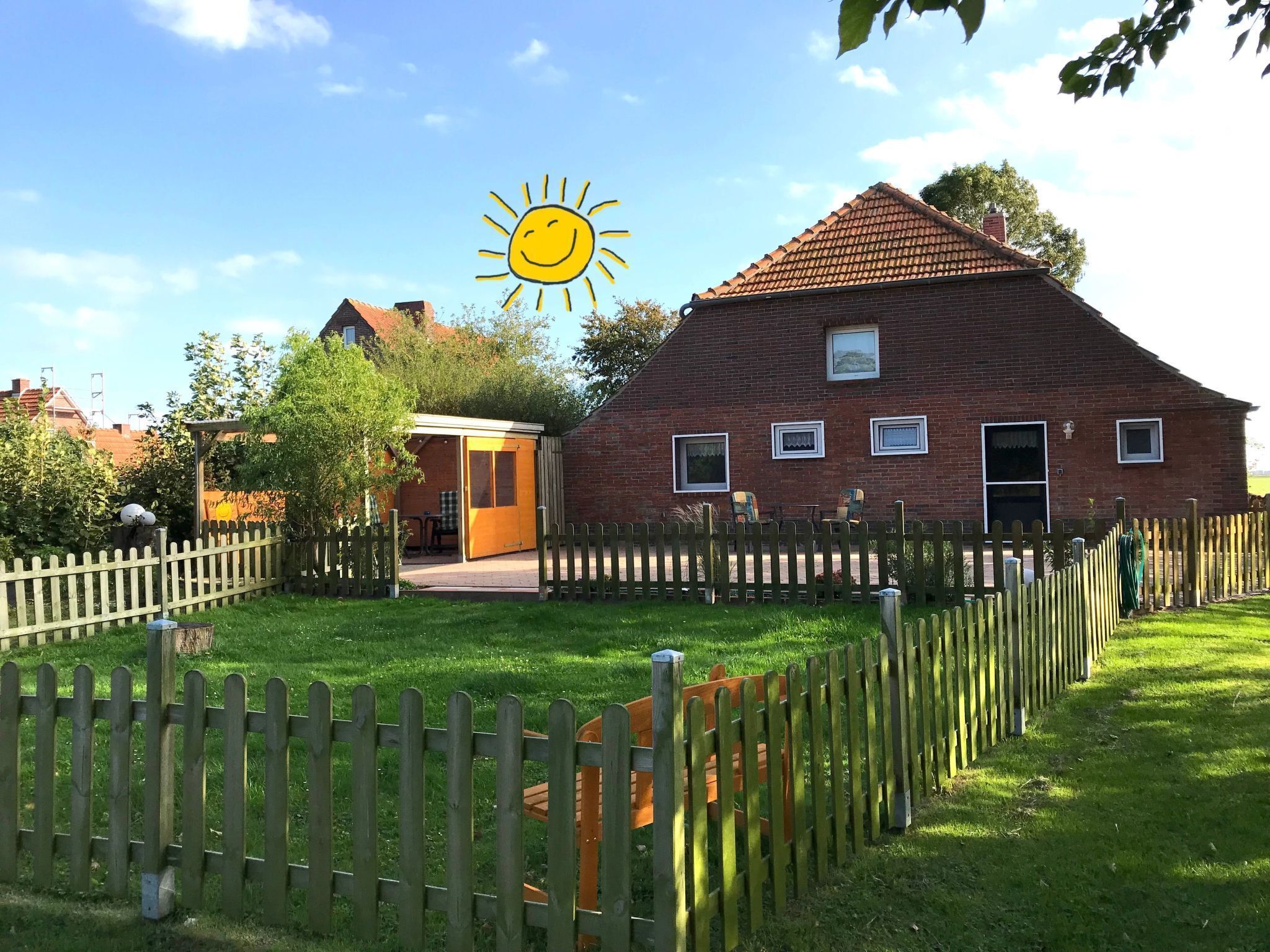 Een stenen huis met een pannendak, een houten omheining en een tuin.