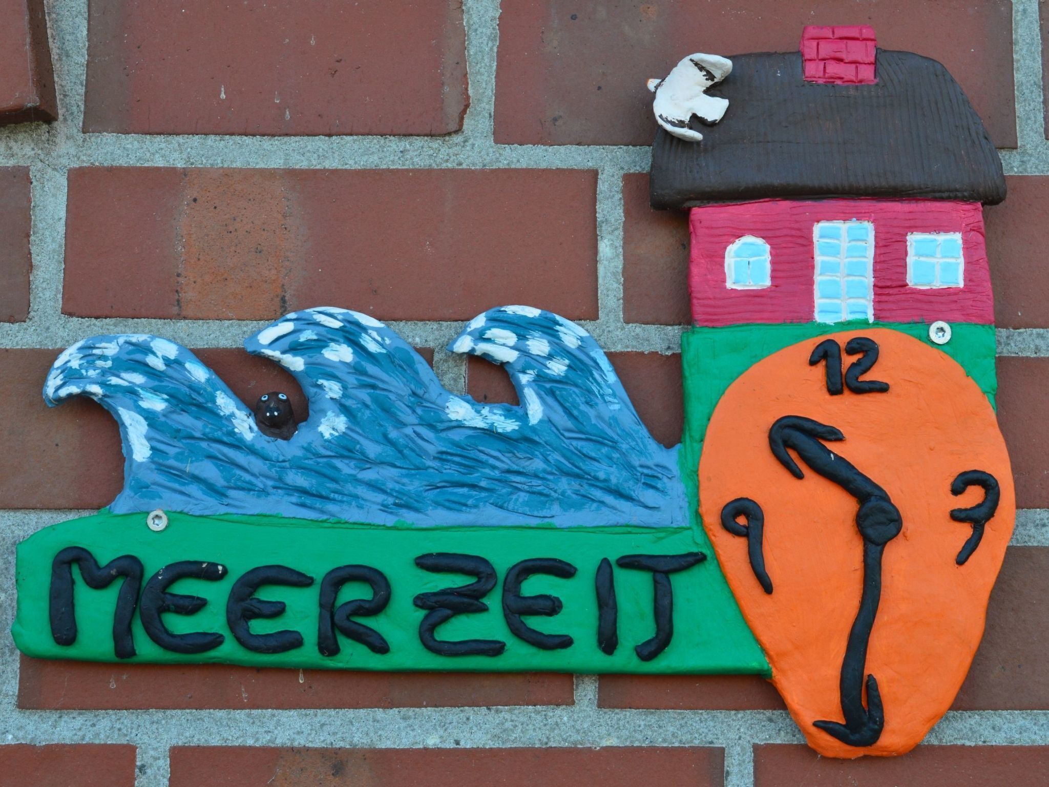 Eine farbenfrohe Wanddekoration mit einem Haus und Wellen, mit dem Schriftzug 'MEERZEIT'.