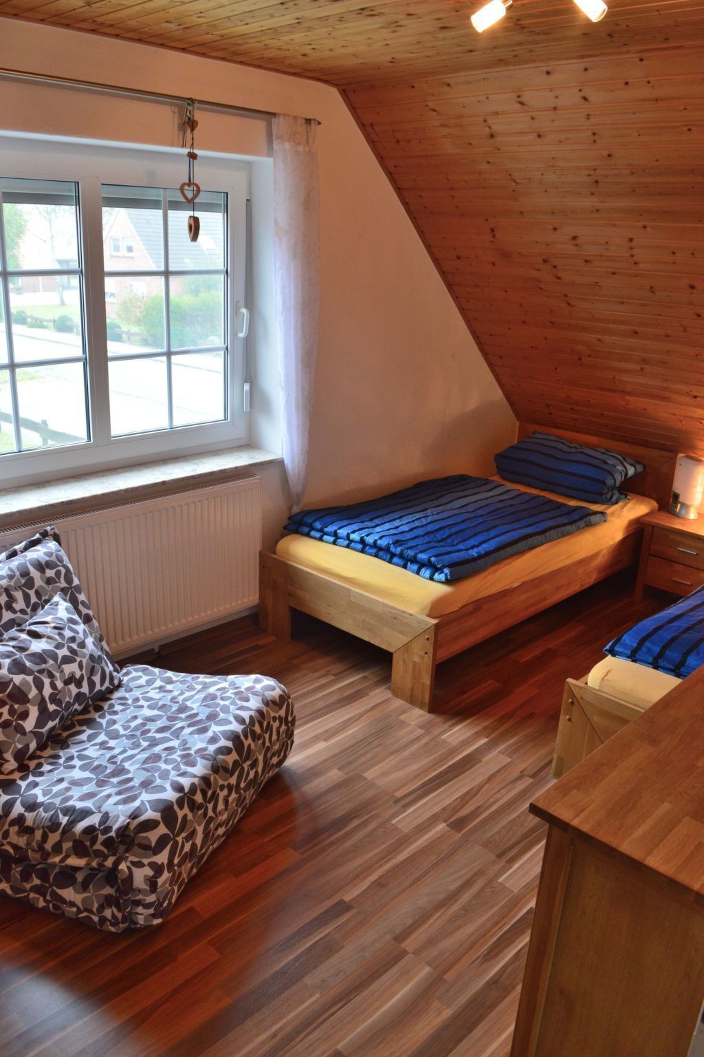 A cozy attic bedroom with a sloped ceiling, a wooden bed, a bench, and a view of the outside.