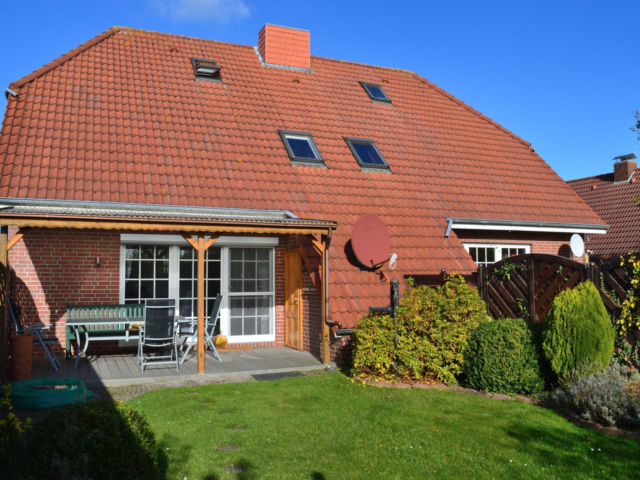 Een huis met twee verdiepingen, voorzien van een rood pannendak, een bakstenen gevel en een veranda met een bankje.