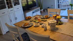 Ein gedeckter Esstisch mit verschiedenen Gerichten, darunter Brot, Salat und einer Obstplatte.