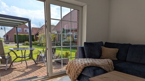 Ein Wohnzimmer mit einem dunkelblauen Sofa, einem Holztisch und einer Glastür, die auf eine Terrasse mit Tisch und Stühlen führt.