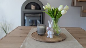 Ein Holztisch mit einer Vase weißer Tulpen, einer Keramik-Hasenfigur und einer Glas-Tasse auf einem runden Holztablett.