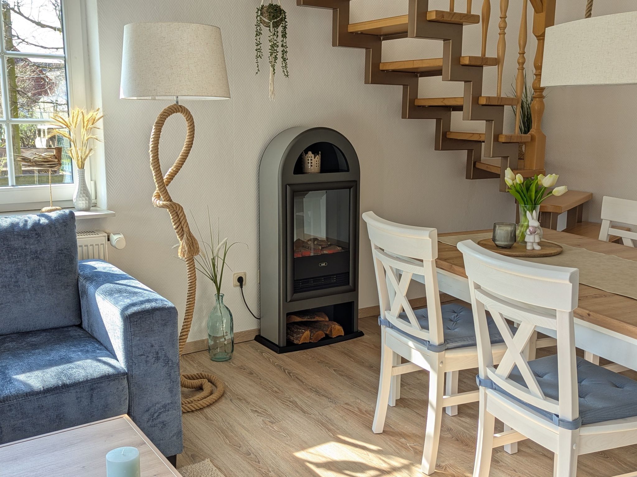 A cozy living room with a fireplace, a blue sofa, wooden dining table, and white chairs.