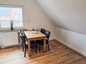A dining area with a wooden table and black chairs, a radiator, a window with a view of buildings, and a potted plant. - Sonnenschein OG by Interhome (Nessmersiel)