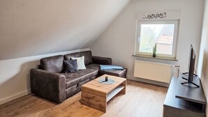 Un salon moderne avec un canapé en cuir marron, une table basse en bois, un meuble TV noir et une fenêtre donnant sur un immeuble.
