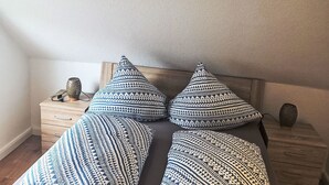 Une chambre à coucher avec une tête de lit en bois, un lit avec une literie à motifs, une table de chevet avec un vase et un petit objet décoratif.