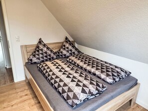 A single bed with a wooden headboard, grey bedding, and patterned pillows in a room with a sloped ceiling. - Sonnenschein OG by Interhome (Nessmersiel)