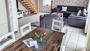 A modern living room with a staircase, a sofa, a dining table with chairs, and a lamp. - Vacation home Max by Interhome (Nessmersiel)
