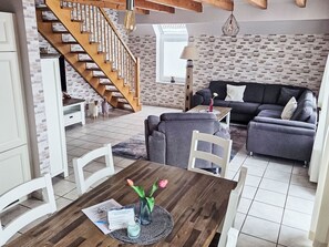 Ein modernes Wohnzimmer mit Treppe, einer Couch, einem Esstisch mit Stühlen und einer Lampe.