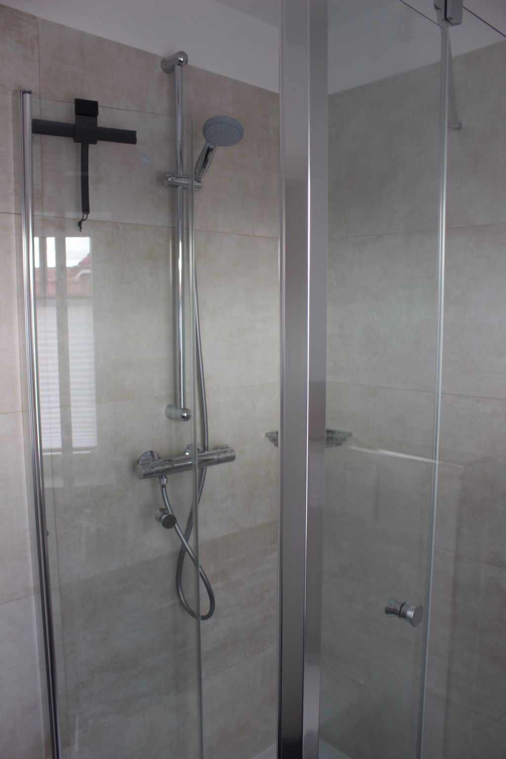Une douche fermée par des parois en verre, dotée d’un pommeau de douche à main, d’un robinet mural et d’un panneau de commande.