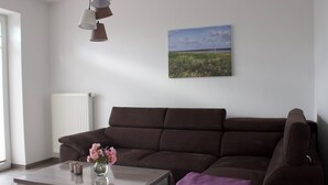 Una sala de estar moderna con un sofá marrón, una mesa de centro blanca con un florero y un cuadro de un paisaje en la pared.