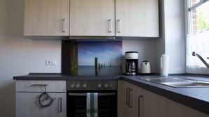 Una cocina moderna con armarios de madera clara, horno empotrado, cafetera y ventana con vistas al mar.