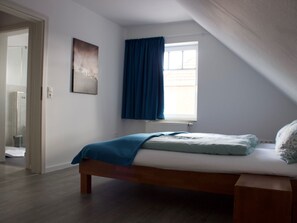 A bedroom with a bed, a window with curtains, a door, and a wall-mounted picture. - Strandflieder by Interhome (Nessmersiel)