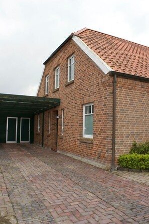 A two-story brick building with a tiled roof, a covered entrance, and a paved driveway. - Strandflieder by Interhome (Nessmersiel)
