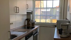 Eine kleine Küche mit weißen Schränken, einer Holz Arbeitsplatte, einem eingebauten Geschirrspüler und einer Kaffeemaschine.