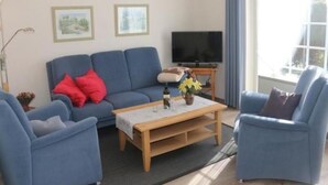 Ein Wohnzimmer mit einem blauen Sofa, einem Holztisch und einem Fernseher.