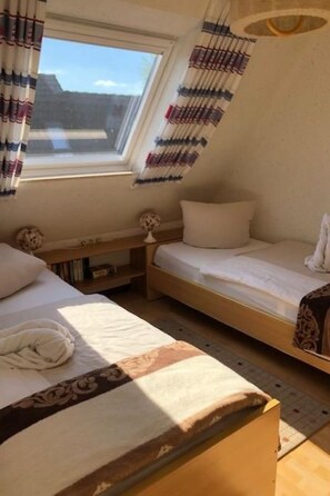 Een compacte kamer met twee bedden, een klein tafeltje en een raam.