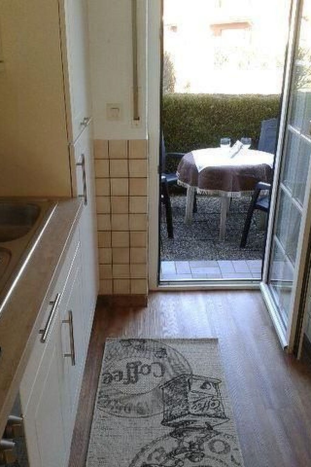 A kitchen with a tiled backsplash, a wooden floor, and a rug with a cartoon character.