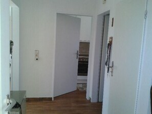 A narrow hallway with wooden flooring, white walls, and a door leading to a room with a built-in oven. - up Acterdeck by Interhome (Nessmersiel)