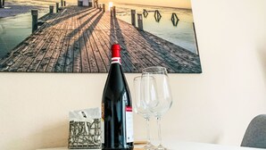 Eine Weinflasche, ein Glas und ein Untersetzer auf einem Tisch mit einem Gemälde von einem Steg und einem Leuchtturm.