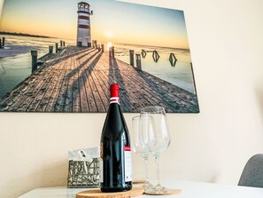 A bottle of wine, a glass, and a coaster on a table with a painting of a pier and lighthouse. - Wohnung mit eigener Terrasse und Panoramablick by Interhome (Nessmersiel)
