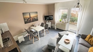 Ein modernes Wohnzimmer mit Essbereich, einem Flachbildfernseher, einem Gemälde und Blick ins Freie.