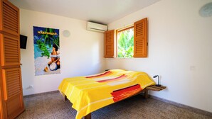 Ein Zimmer mit einem Bett, einem Poster, einem Fenster mit Fensterläden und einer Klimaanlage.