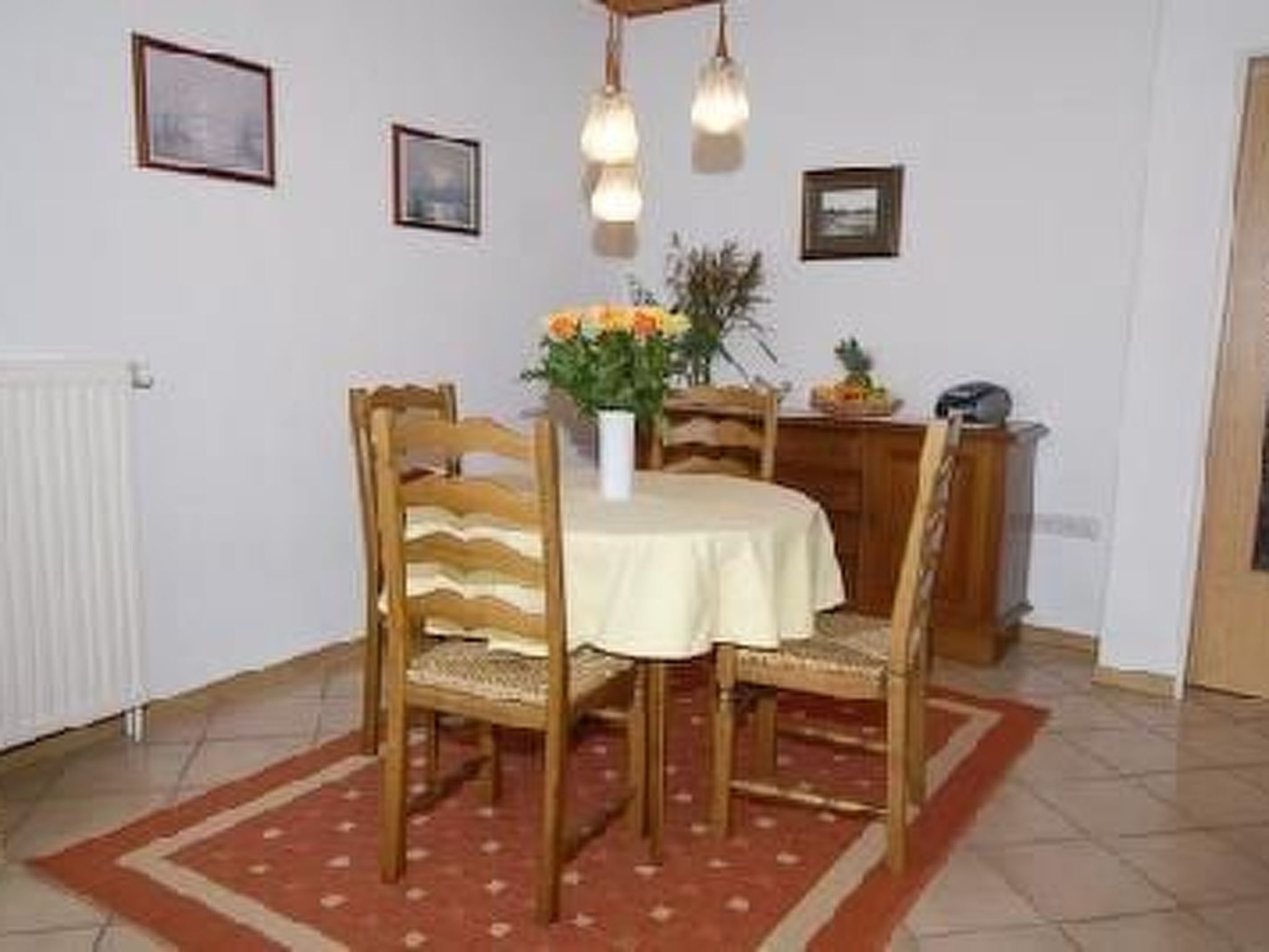 Ein Essbereich mit einem runden Tisch, vier Holzstühlen, einer Vase mit Blumen und Wandleuchten.