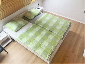 Ein Zimmer mit einem Einzelbett, Holzboden, weißem Kopfteil und Nachttisch mit Lampe.