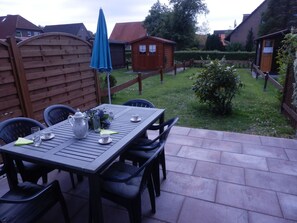 Eine Terrasse mit Tisch für vier Personen, umgeben von Stühlen und einem blauen Sonnenschirm.