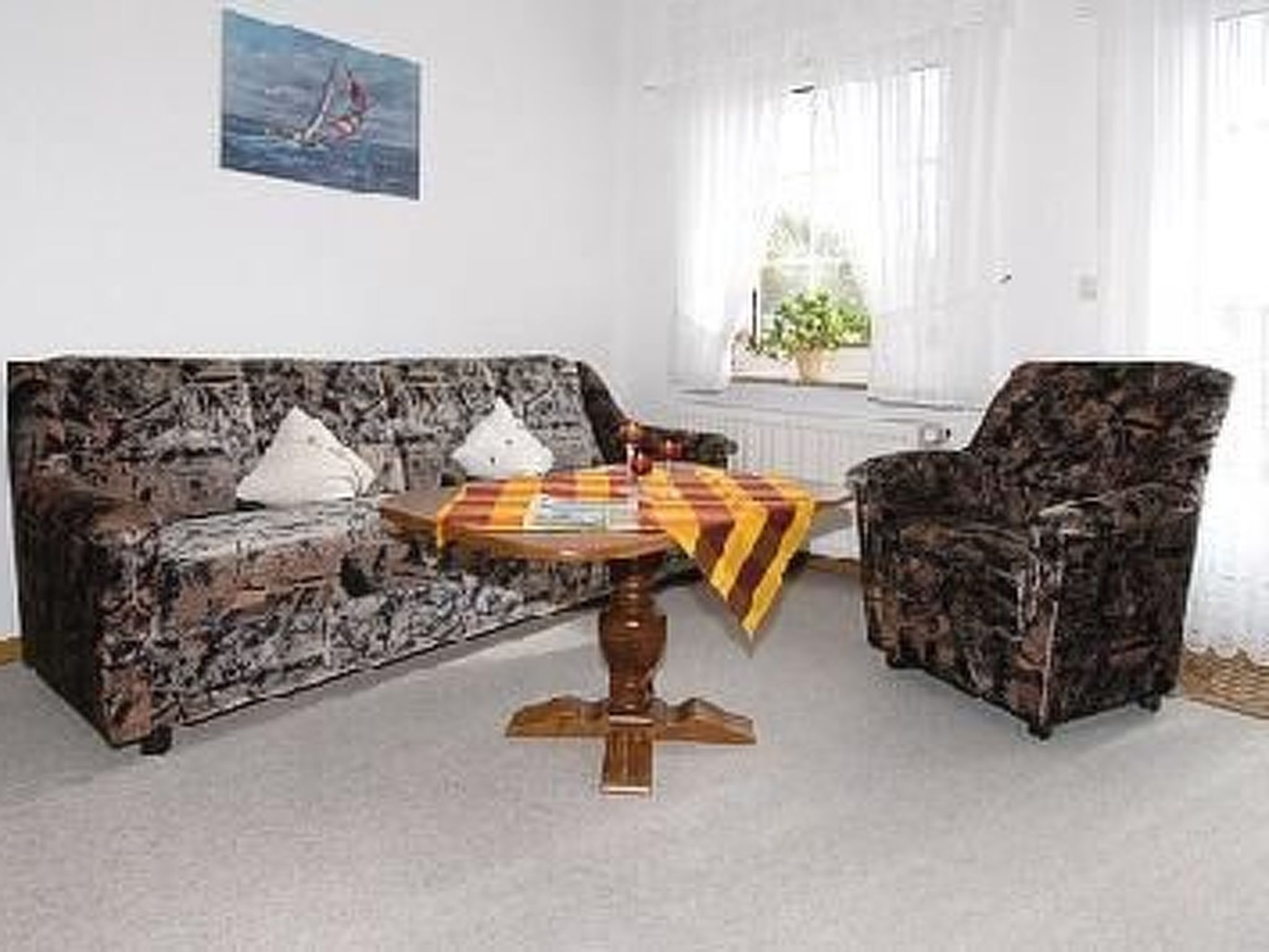 Une pièce avec un canapé à motifs, un fauteuil assorti et une petite table ronde recouverte d’une nappe à carreaux.