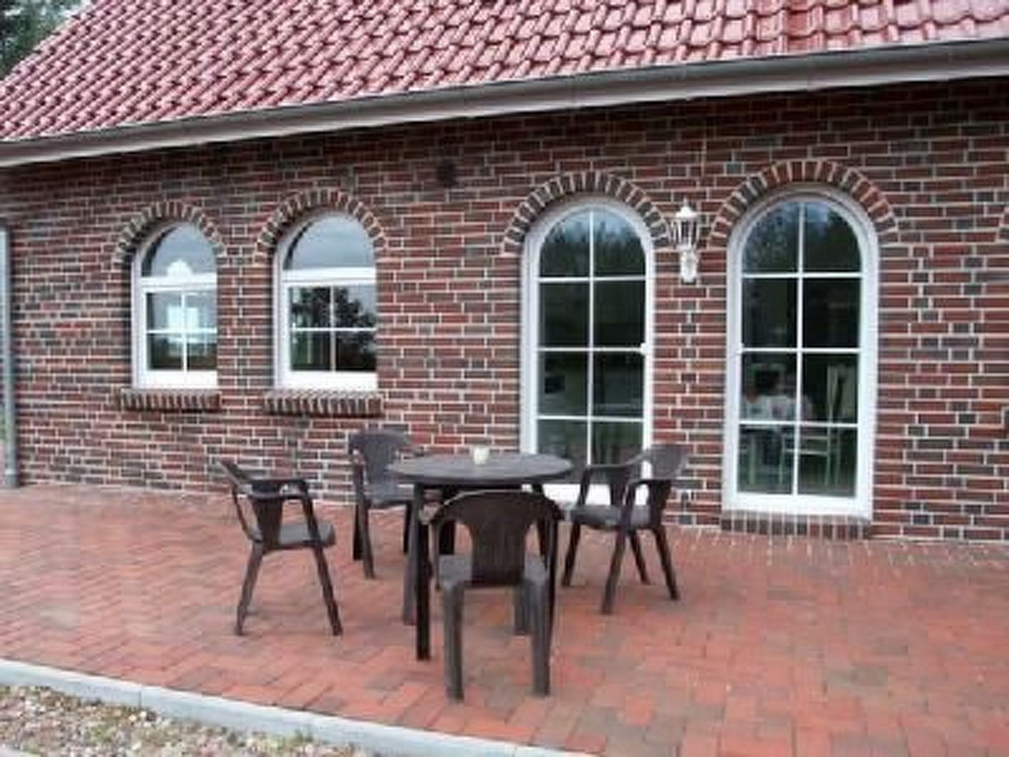 Un edificio de ladrillo con tejado de baldosas, tres ventanas de arco y un patio con mesa y sillas.