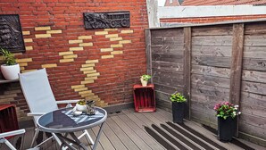 Eine Terrasse mit einem runden Tisch und Stühlen, eine Backsteinmauer mit gelbem Muster und ein Holzzaun.