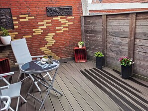 Un patio con una mesa redonda y sillas, un muro de ladrillo con un diseño amarillo y una cerca de madera.