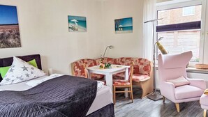 Ein Schlafzimmer mit einem Bett, einem Schlafsofa, einem Sessel, einem Tisch und einem Fenster.