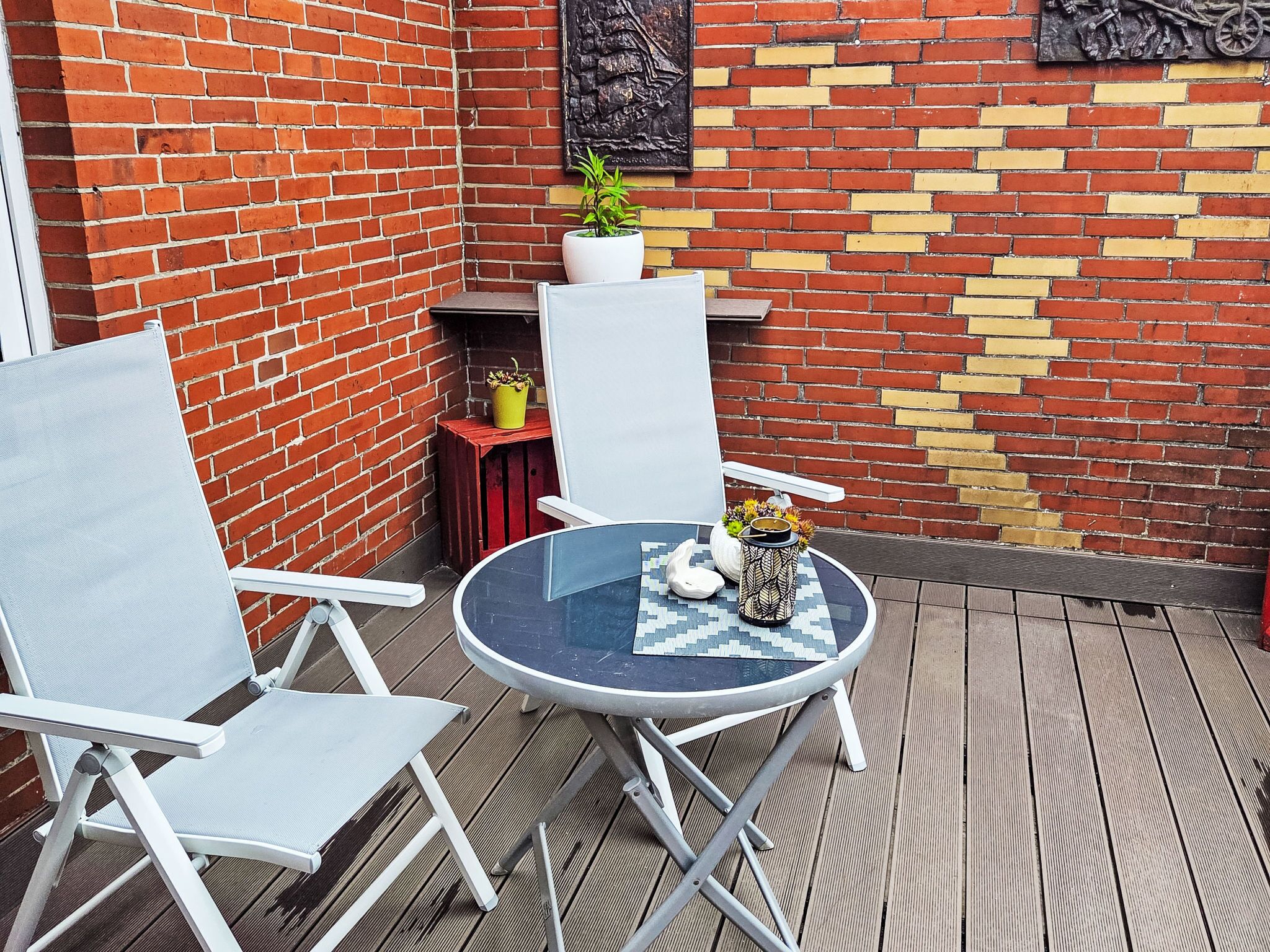 A patio area with a round table, two chairs, a potted plant, and a decorative wall.