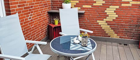 A patio area with a round table, two chairs, a potted plant, and a decorative wall.