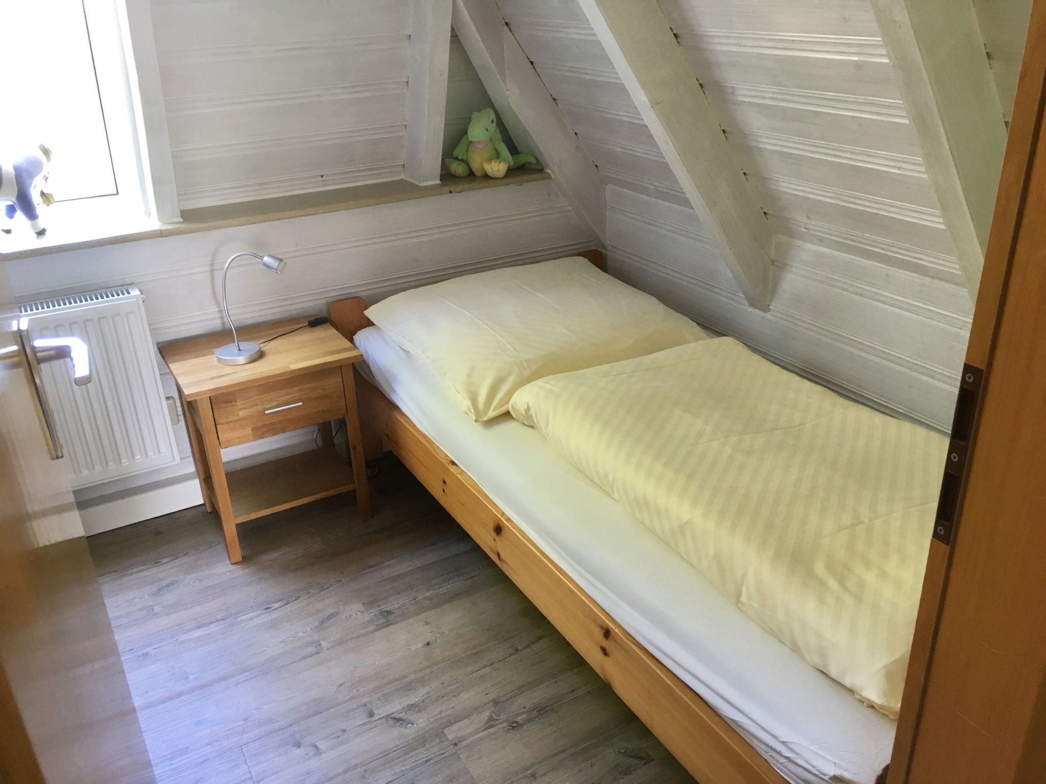 Une petite chambre avec un lit simple, un bureau en bois et un radiateur.