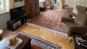 Een ruime woonkamer met een grote flatscreen-tv, een houten kast en een rood tapijt met een patroon.