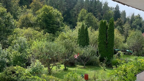 Een balkon met uitzicht op een verzorgde tuin met verschillende bomen en struiken.