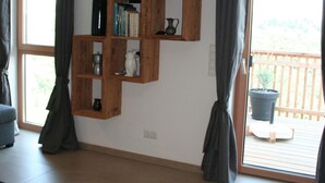 Una habitación con una estantería de madera, un ventanal con cortinas y una planta en maceta en un balcón.
