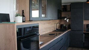 Una cocina moderna con armarios oscuros, encimera de madera, horno empotrado y refrigerador negro.