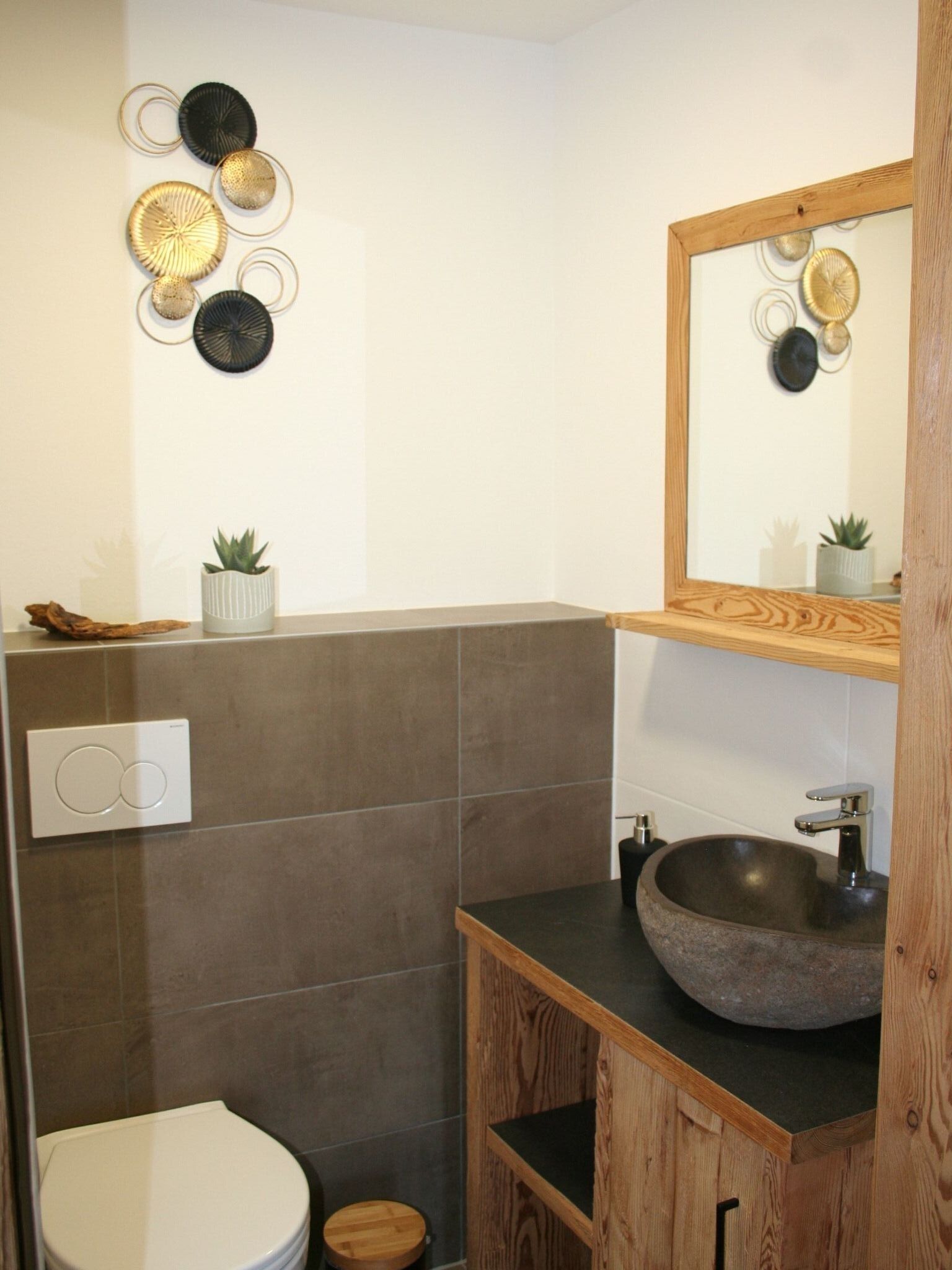 A modern bathroom with a stone sink, wooden vanity, and a toilet.
