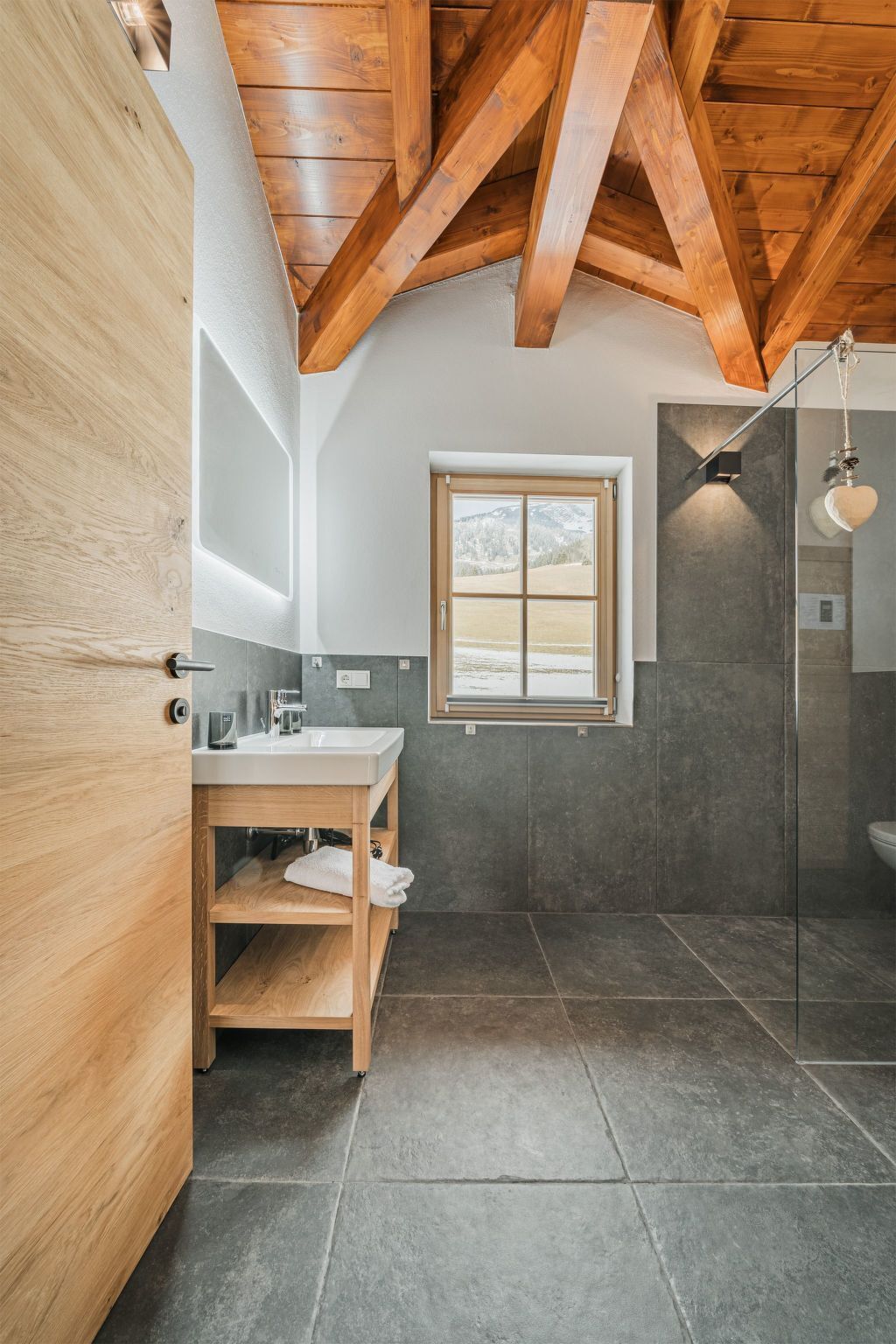 A modern bathroom with a wooden ceiling, a large window, a glass shower, and a wooden vanity.