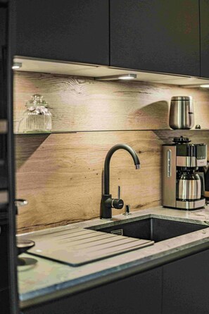 Eine moderne Küche mit einem eleganten schwarzen Wasserhahn, einer Edelstahl-Kaffeemaschine und einer Holzrückwand.