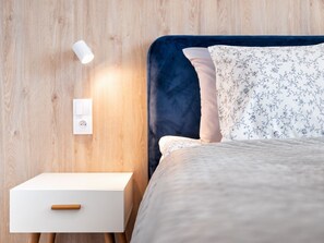 Ein ordentlich bezogenes Bett mit Blumenmuster, ein dunkelblaues Kopfteil und ein weißer Nachttisch mit Holzgriff.