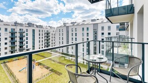 Ein Balkon mit Glastisch und Stühlen, mit Blick auf einen Spielplatz und eine Wohngegend.